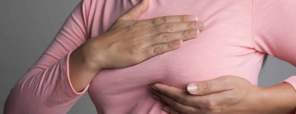 Woman hand checking lumps on her breast for signs of breast cancer on gray background. Healthcare concept.